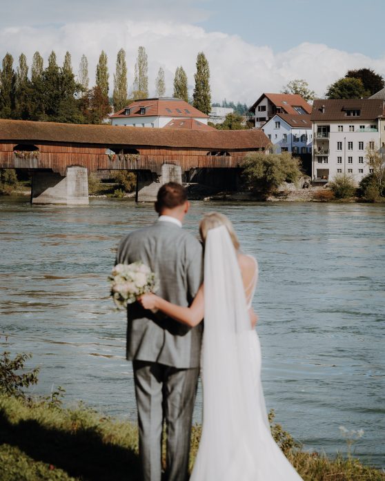 Das Brautpaar steht verliebt vor einem großen Fluss