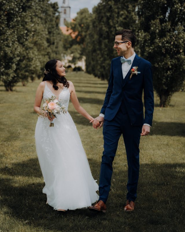 Ein Brautpaar läuft Hand in Hand auf einer grünen Wiese