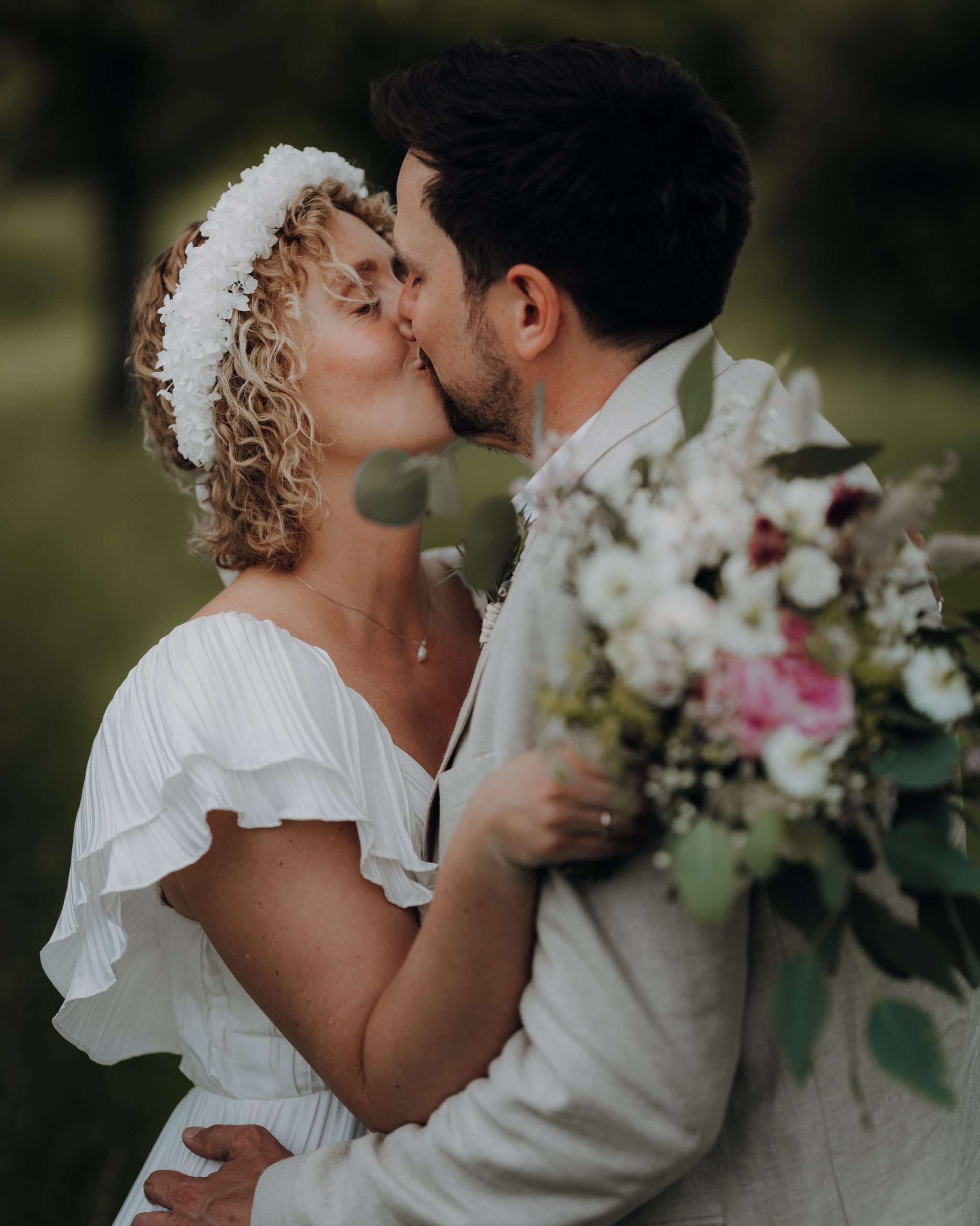 Der Bräutigam küsst seine Braut während Sie den Brautstrauss hält