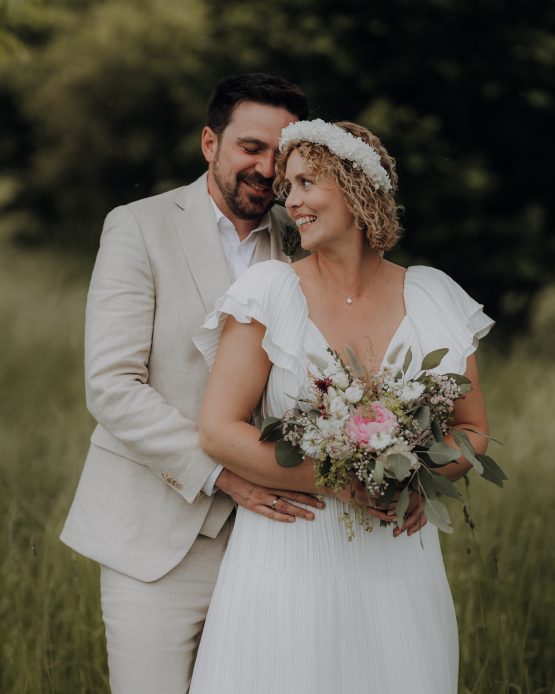 Ein Brautpaar steht vor einem Wald und lächelt sich an